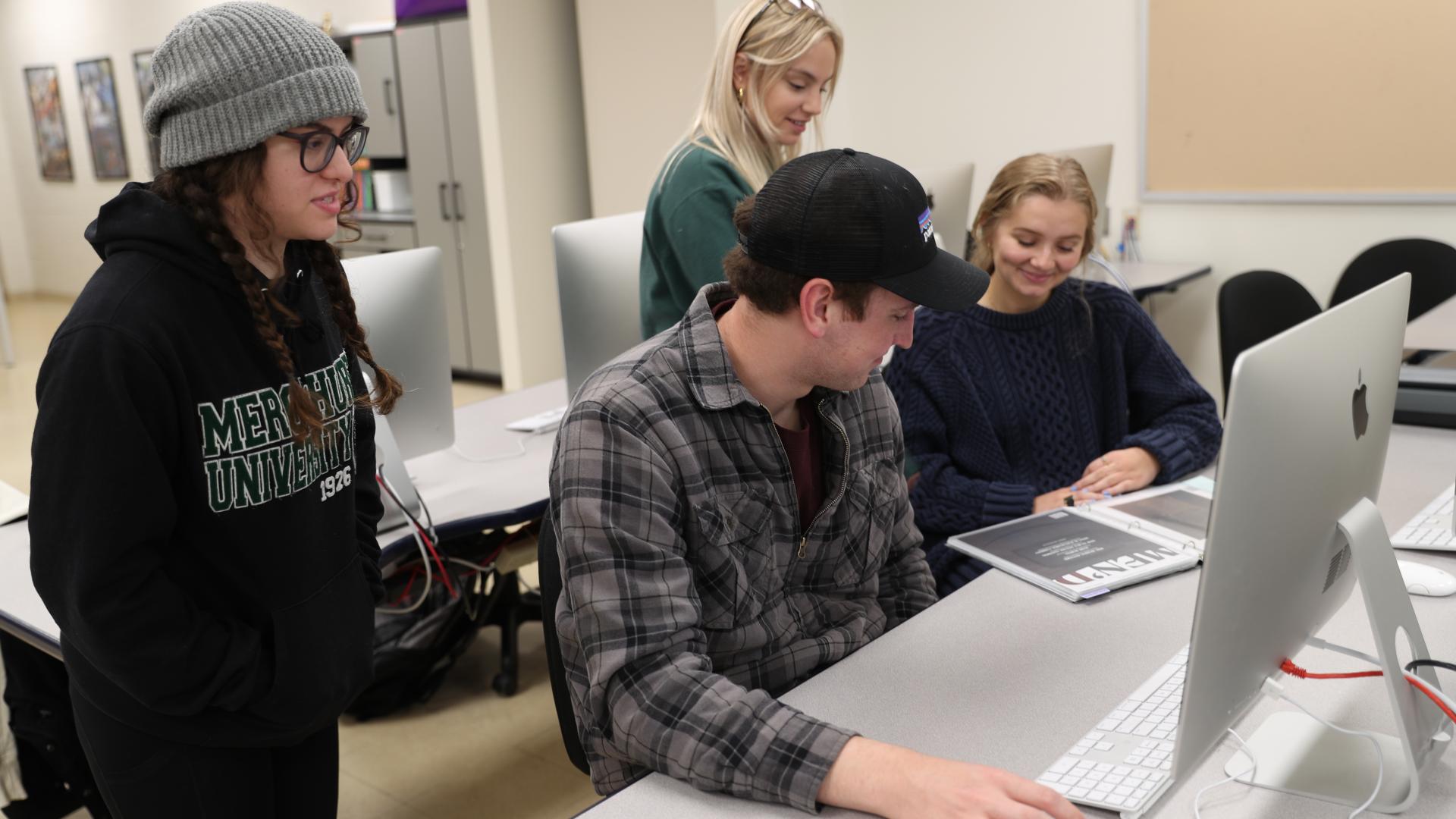  group of graphic design students gather around a computer