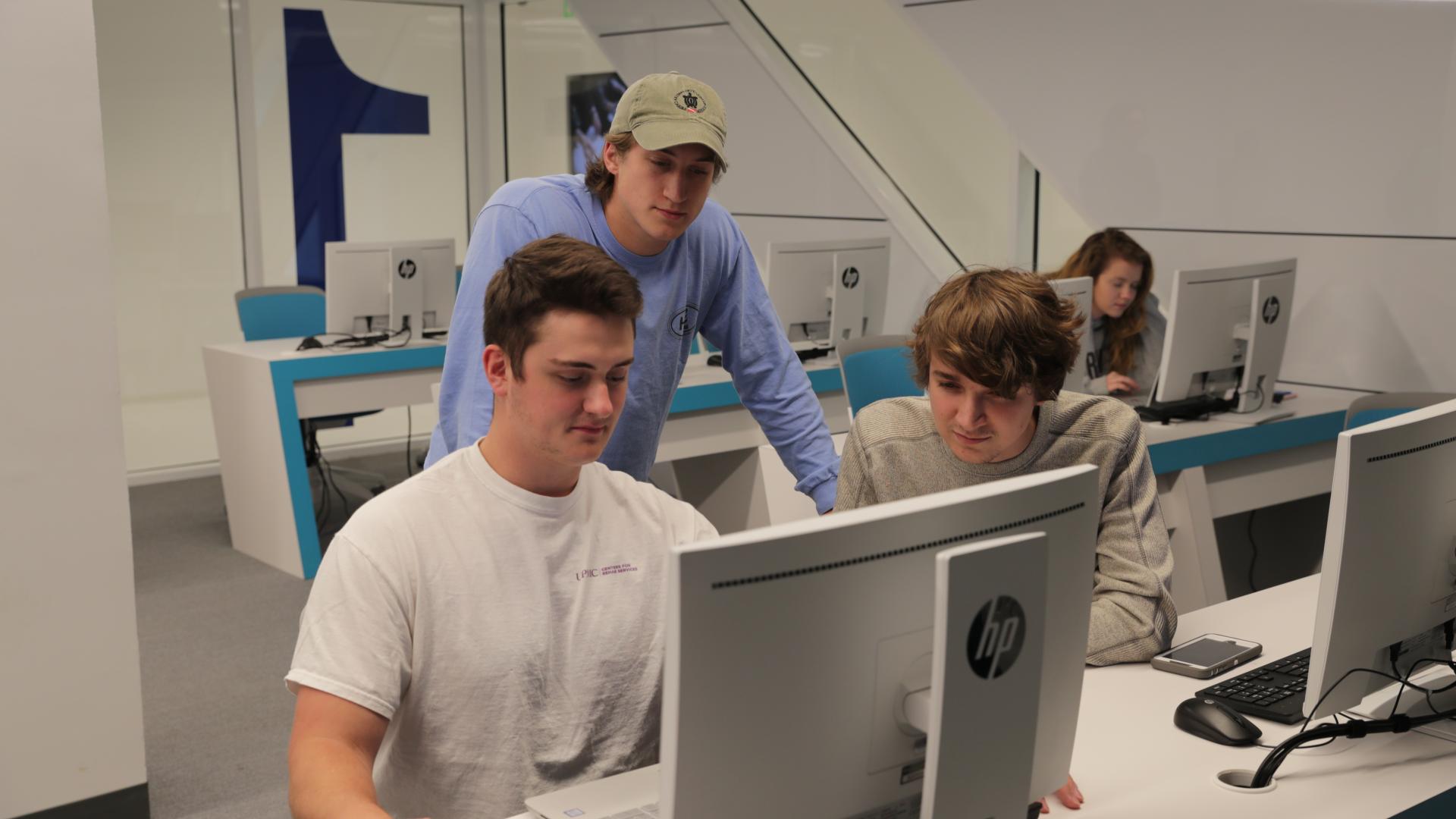 three male students gather around a computer in a cyber lab