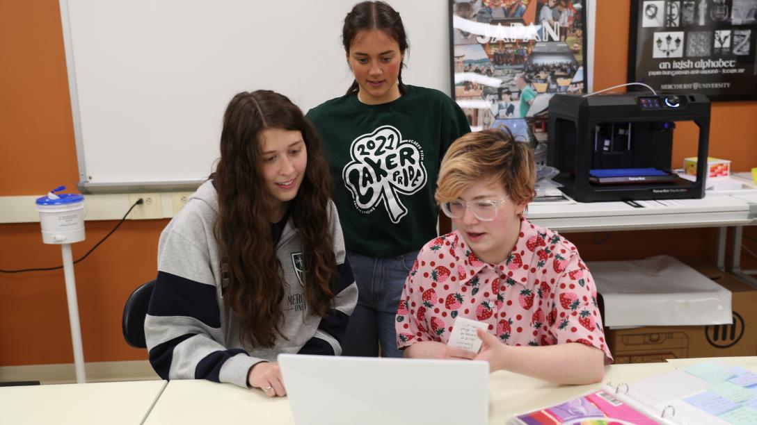 three female students gather around a computer
