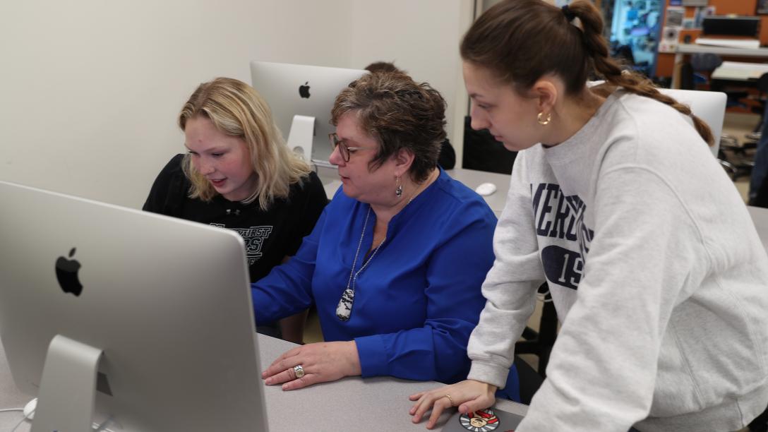 a professor and two female students around a computer