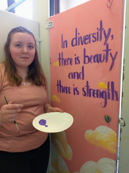female student painting mural stops for a photo